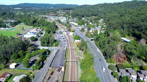 Landscape-shot-of-cars-driving-on-main-town-road-street-with-train-station-railway-shops-bushland-suburbs-Ourimbah-Central-Coast-Australia-drone-aerial