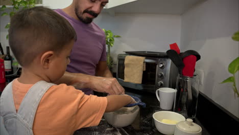 Cámara-Lenta-De-Un-Padre-Latino-Mexicano-Con-Una-Camisa-Morada-Haciendo-Galletas-Con-Su-Hijo-Tamizando-Harina-Con-Los-Dedos-Haciendo-Un-Desastre-En-La-Cocina