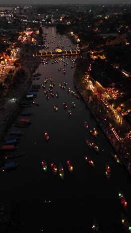 Vista-Aérea-De-Impresionantes-Barcos-Iluminados-En-El-Río-Hoai-Durante-La-Celebración-Del-Barco-Hoi-An-Linterna,-Vídeo-Vertical