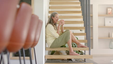 A-mature-Caucasian-woman-with-grey-hair-sits-on-stairs,-holding-cup