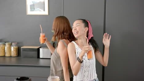 Two-young-biracial-female-friends-enjoy-drinks-and-a-dance-in-a-kitchen