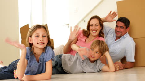 Happy-family-lying-on-floor-in-their-new-home-waving-at-camera