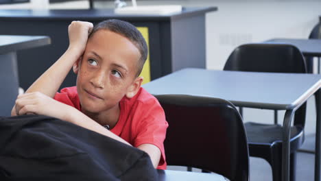 Biracial-boy-with-freckles-sits-thoughtfully-in-a-classroom-in-school