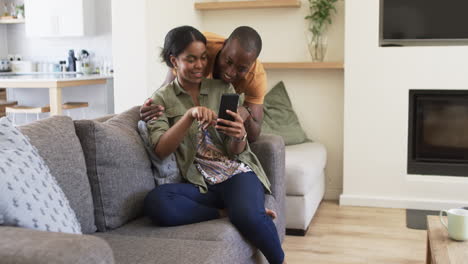 A-young-African-American-couple-is-sharing-a-moment-on-the-sofa,-looking-at-a-smartphone