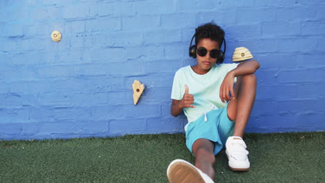 In-a-school-setting,-an-African-American-boy-relaxes-against-a-blue-wall-with-copy-space