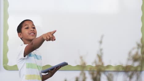 Biracial-boy-focused-on-using-a-smartphone,-standing-in-a-classroom-in-school-with-copy-space