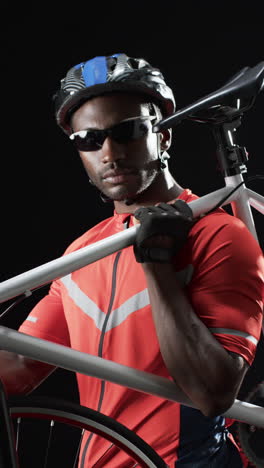 Vertical-video:-African-American-male-athlete-holding-bicycle,-black-background