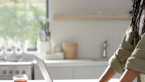 African-American-young-woman-wearing-green-shirt-using-laptop-in-kitchen