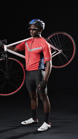 Vertical-video:-African-American-male-athlete-holding-red-and-black-bicycle,-black-background