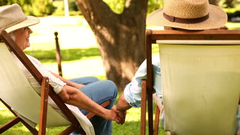 Retired-couple-sitting-in-deck-chairs-holding-hands