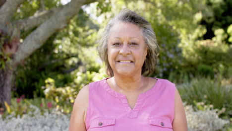 Biracial-senior-woman-standing-in-sunny-garden,-smiling-at-camera