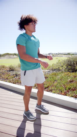 Vertical-video:-A-young-biracial-male-standing-on-a-wooden-walkway,-with-a-blue-sky-background