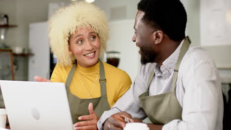 Barista-team-of-an-African-American-man-and-biracial-woman-wearing-aprons-using-laptop