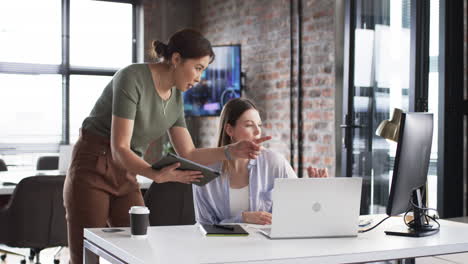 Asian-elder-shows-screen,-young-Caucasian-colleague-observes