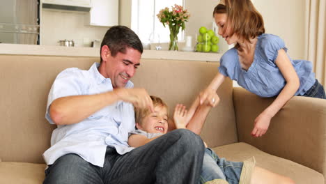 Father-and-daughter-tickling-little-boy-in-the-couch