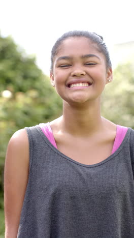 Vertical-video:-Biracial-young-girl-wearing-gray-tank-top,-smiling-outdoors