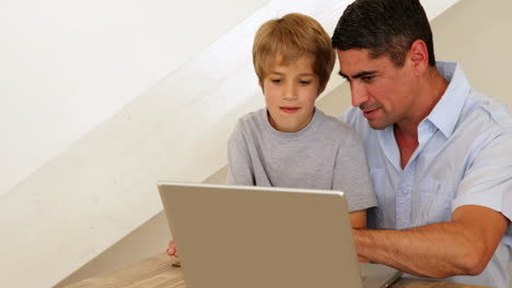 Niño-Usando-Una-Computadora-Portátil-Con-Su-Padre-En-La-Mesa