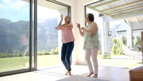 Asian-grandmother-and-biracial-granddaughter-are-dancing-together-in-bright-room
