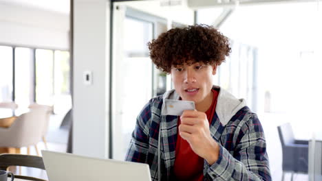 A-young-biracial-man-shopping-online-with-credit-card-and-laptop-with-copy-space-at-home