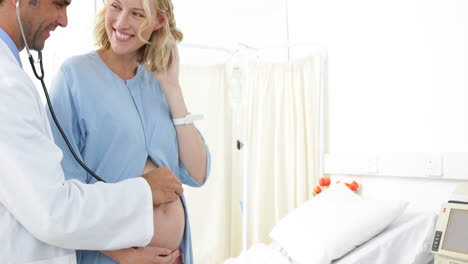 Pregnant-woman-standing-in-hospital-gown-being-checked-by-doctor