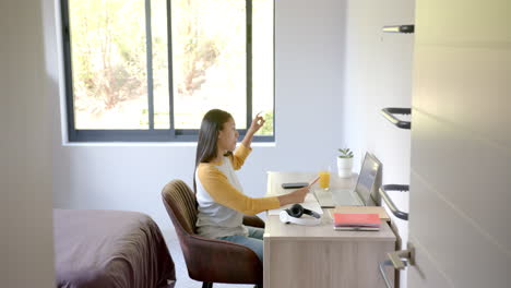 A-biracial-young-woman-is-sitting-at-desk,-looking-at-a-laptop