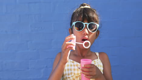 In-school,-a-young-biracial-student-blows-bubbles-against-a-blue-background