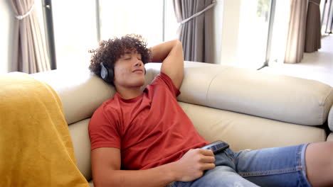 A-young-biracial-man-relaxes-on-a-sofa-at-home-with-headphones