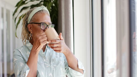 African-American-senior-woman-holding-cup,-looking-out-window