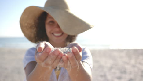 A-young-biracial-woman-is-holding-sand-in-her-hands-at-the-beach