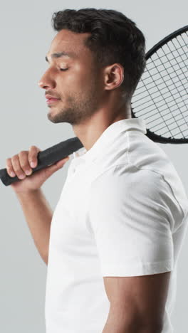 Vertikales-Video:-Gemischtrassiger-Männlicher-Athlet-Hält-Tennisschläger,-Grauer-Hintergrund