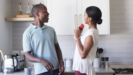 A-diverse-couple-shares-a-joyful-moment-in-the-kitchen,-surprising-with-gifts