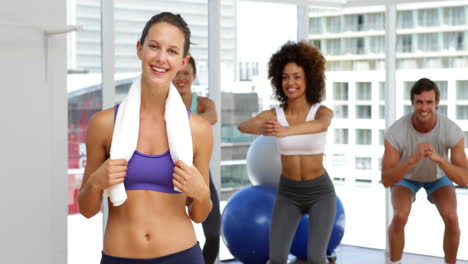 Fitness-class-squatting-on-bosu-balls-while-instructor-smiles-at-camera