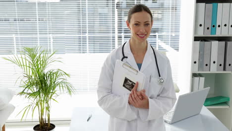 Doctor-leaning-on-desk-smiling-at-camera