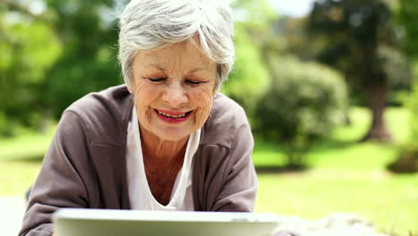 Glückliche-ältere-Frau-Entspannt-Sich-Im-Park-Mit-Ihrem-Tablet