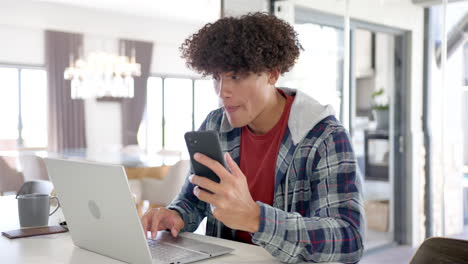 A-young-biracial-man-is-using-his-smartphone-and-laptop-at-home