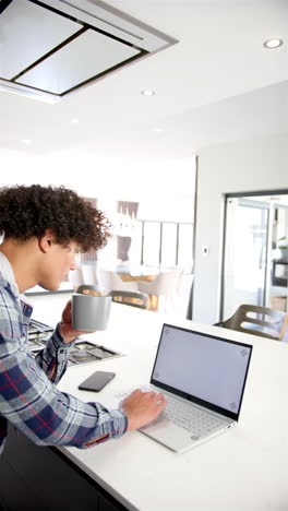 Vertical-video:-A-young-biracial-man-is-working-on-a-laptop