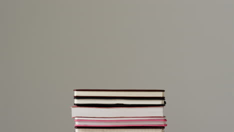 A-stack-of-various-hardcover-and-paperback-books-sits-against-a-neutral-background,-with-copy-space