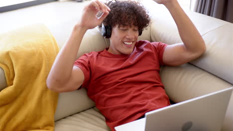 A-young-biracial-man-relaxes-on-a-sofa-at-home-with-headphones
