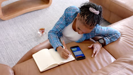 African-American-young-woman-wearing-blue-plaid-shirt,-writing-in-a-notebook