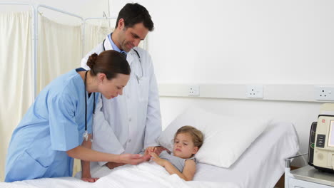 Sick-little-girl-lying-in-bed-talking-to-nurse-and-doctor