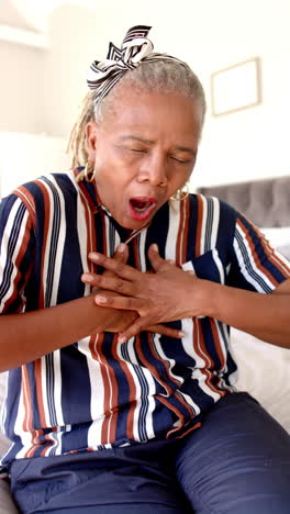 Vertical-video:-African-American-senior-woman-sitting,-appears-to-be-coughing