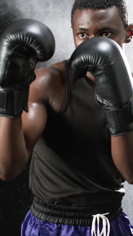 Vertical-video:-African-American-male-athlete-wearing-boxing-gloves,-black-background