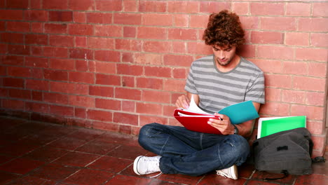 Student-sitting-against-wall-reading-textbook