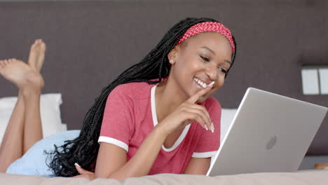 African-American-young-woman-lying-on-bed,-looking-at-laptop