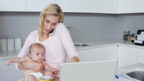 Madre-Haciendo-Una-Llamada-Telefónica-Y-Sosteniendo-A-Un-Bebé