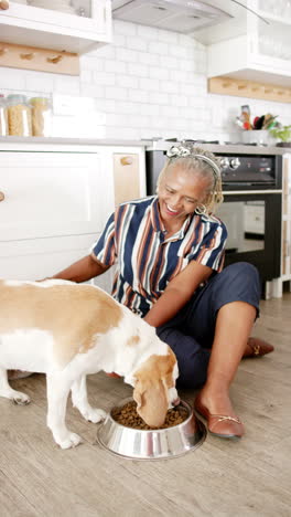 Vertical-video:-African-American-senior-woman-petting-her-dog-in-kitchen