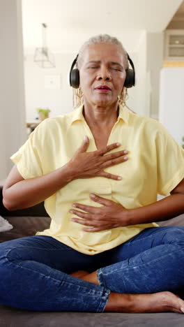 Vertical-video:-Elderly-African-American-woman-closes-eyes,-enjoys-music,-hand-on-chest