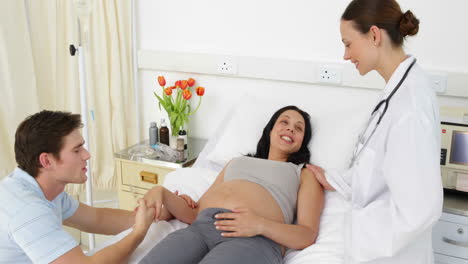 Brunette-pregnant-woman-lying-on-bed-talking-with-partner-and-doctor