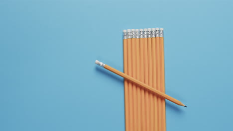 A-single-yellow-pencil-lies-across-a-neat-row-of-pencils-on-a-blue-background