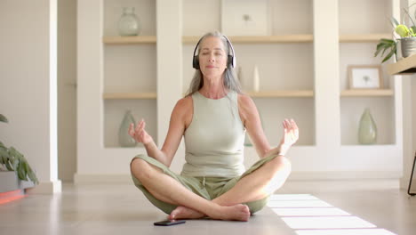 Caucasian-woman-with-gray-hair-meditating,-wearing-headphones
